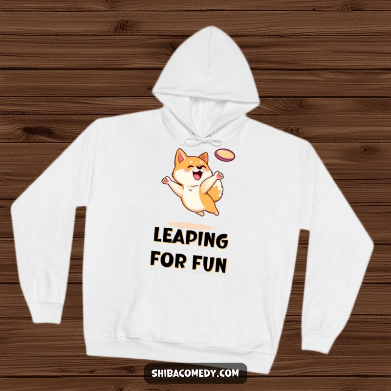Funny Shiba Inu dog character leaping for a frisbee on a cozy hoodie, perfect for staying warm and playful.